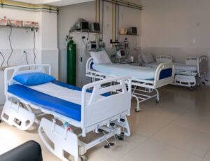 Hospital ward with two adjustable patient beds, blue bedding, and medical monitors along the wall.